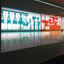 A brightly lit art installation in a corporate training room showcases abstract silhouettes of various robotic arms and machinery in turquoise and red colors, displayed on a sleek white wall enhanced by an LED system for stunning backlit wall art. The glossy floor reflects the vivid shapes brilliantly.