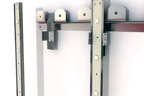 Metal brackets and rails attached to a wall, likely part of a mounting system. The units have rectangular holes and hooks, suggesting they are designed to support or hang other objects. The background is white, highlighting the metallic components.