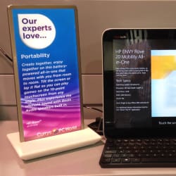 A display of an HP Envy Rove 20 Mobility All-in-One computer on a store counter. Next to it, there is a sign that highlights the portability of the device, with text mentioning its battery power and tilt functionality. The display is from Currys PC World.