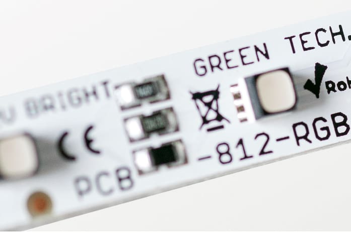 Close-up view of a white LED strip labeled "GREEN TECH" with various small electronic components and symbols, including a checkmark symbol and text "812-RGB" on a white background.