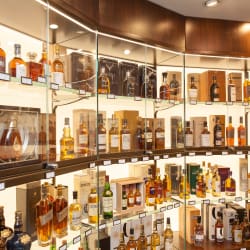 A well-lit shop showcasing a variety of spirits, including whiskey, vodka, and wine. Shelves with Bright Green technology LED shelf lighting and tables are stocked with bottles, boxes, and gift sets.