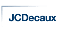 Logo of JCDecaux, featuring the company name in bold blue letters with a thin, horizontal, silver line extending above and to the left, forming an incomplete rectangle around the text. The background is transparent.