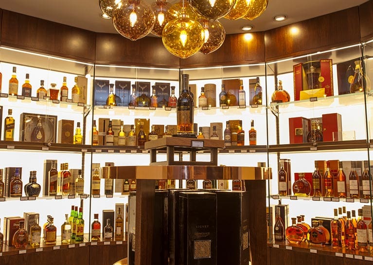 A well-lit shop showcasing a variety of spirits, including whiskey, vodka, and wine. Shelves with Bright Green technology LED shelf lighting and tables are stocked with bottles, boxes, and gift sets.