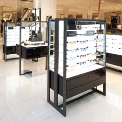 A bright, modern store interior at David Clulow at Selfridges London features display cases filled with various styles of eyeglasses and sunglasses. Bright Green Technology delivered 16 custom Light Panels in just 10 days, enhancing the backlit shelves that showcase the eyewear attractively.