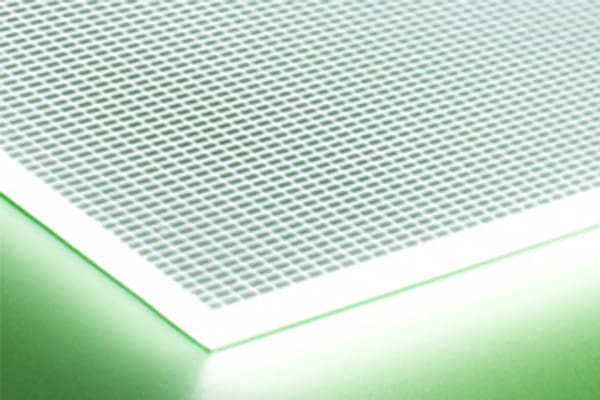 A close-up view of an illuminated, translucent surface with a grid-like pattern, glowing with green light. The corner of the surface is prominently visible, and the light reflection creates a gradient effect on the surrounding area.