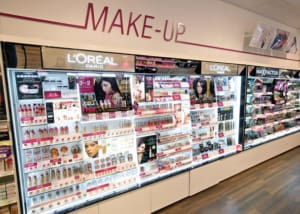 A brightly lit makeup section in a store featuring various cosmetics from L'Oréal Paris and Max Factor. The LED light sheet panels enhance the shelves illumination, showcasing well-stocked products like lipsticks, foundations, and mascaras arranged in neat, colorful displays.