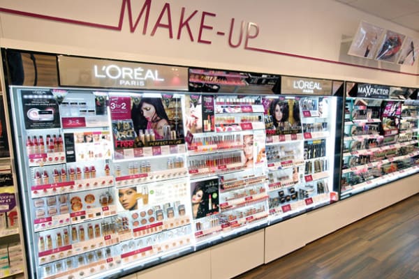 A brightly lit makeup section in a store featuring various cosmetics from L'Oréal Paris and Max Factor. The LED light sheet panels enhance the shelves illumination, showcasing well-stocked products like lipsticks, foundations, and mascaras arranged in neat, colorful displays.