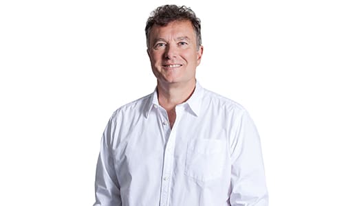 A man with short, curly hair is smiling at the camera. He is wearing a white button-up shirt and is standing against a plain white background.