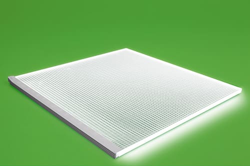 A square LED panel light with a grid-like surface is set at an angle, illuminating against a bright green background. The light panel appears sleek and modern, emitting a soft white glow.