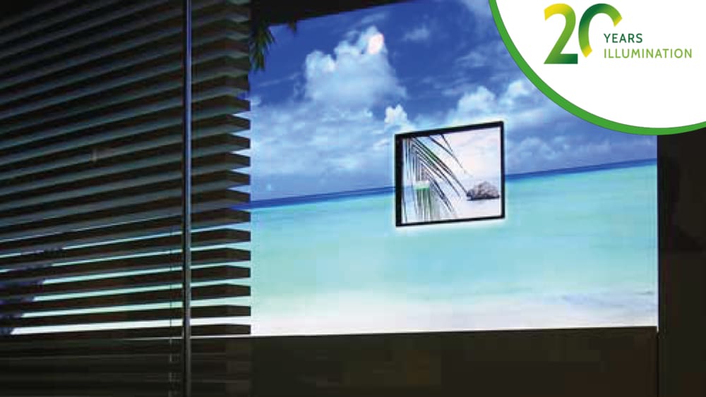 A window with horizontal blinds partially open reveals a sunny beach scene with blue water and a small island in the background. A small framed image of a palm tree leaf sits adjacent to an LED lightbox displaying a green and white logo that reads "20 Years Illumination.